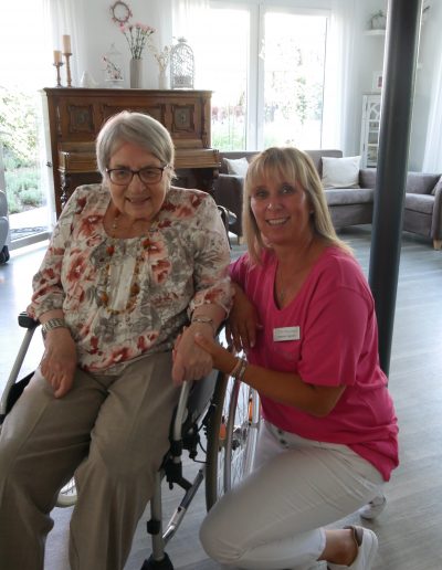 Seniorin im Rollstuhl, daneben kniend die Pflegerin